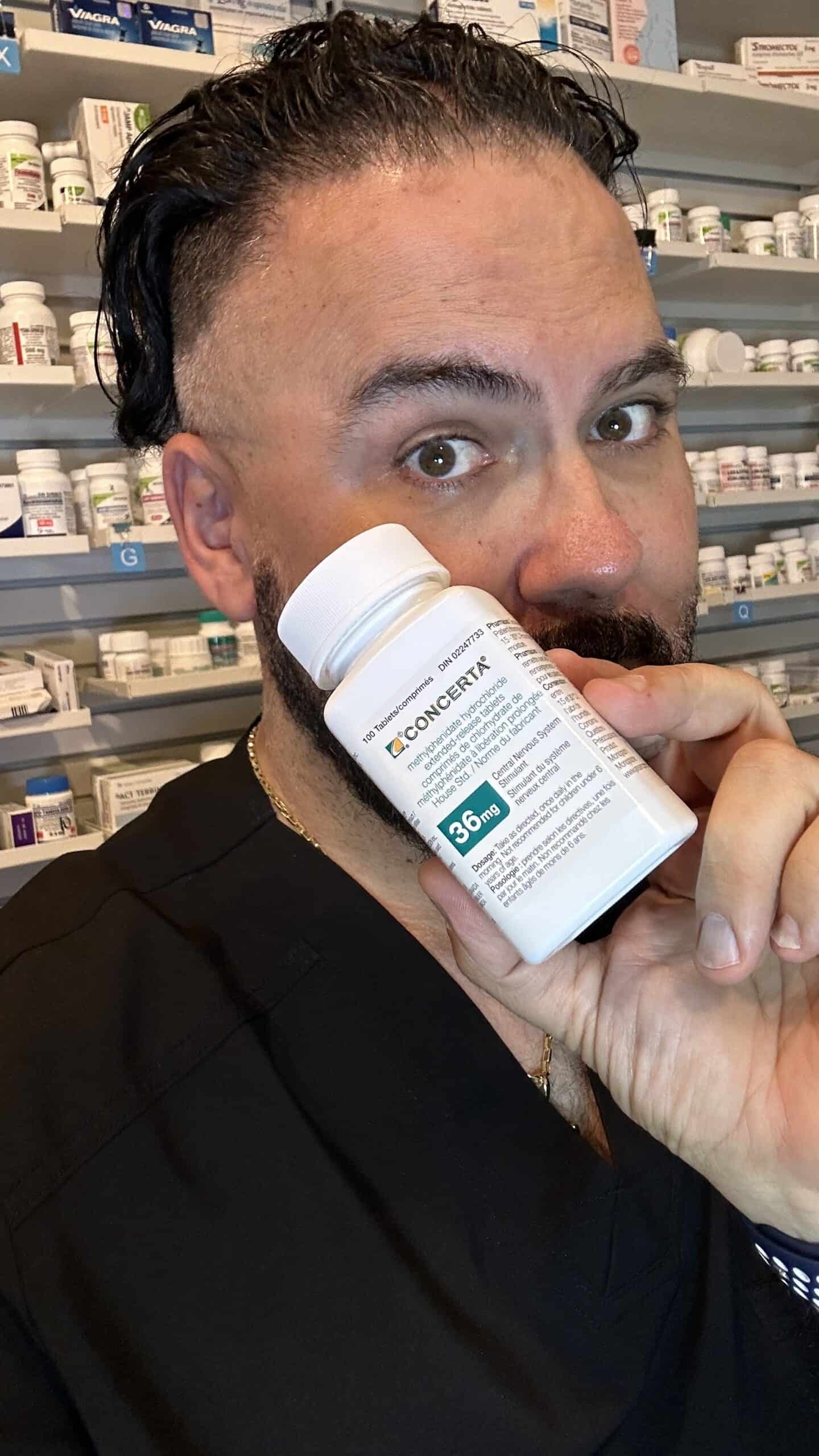 MisterPharmacist_Toronto_Online_Pharmacy A person with dark hair holds a bottle of Concerta 36 mg, surrounded by pharmacy shelves brimming with various ADHD medication boxes. They are wearing a black shirt.