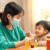 A smiling parent giving medicine to a child using a colorful spoon, with bright medicine bottles on a table in a cozy home setting.