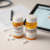 Close-up of Vyvanse and Concerta prescription bottles on a white surface with a blurred prescription pad and digital tablet in the background.