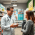 A pharmacist in a modern pharmacy explaining medication to a patient, with shelves of medicines and health posters about chronic disease and vaccin...