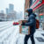 Snowy Toronto street with heavy snowfall, a delivery person in winter gear carrying a pharmacy package, and a pharmacy storefront in the background.