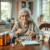 Elderly woman organizing medications at a kitchen table with pill organizer, medication bottles, glass of water, and a calendar in a cozy kitchen.