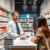 A modern pharmacy counter with a pharmacist consulting a patient, surrounded by medication shelves and digital health icons symbolizing prescriptio...