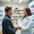 A modern pharmacy interior with a pharmacist consulting a young adult about acne treatment, bright setting with skincare products on shelves.