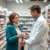 A pharmacist in a modern pharmacy assisting a patient with flu medication, surrounded by shelves of medicine and health products.