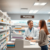 Bright modern pharmacy interior with shelves of medications and a friendly pharmacist consulting a patient over the counter.