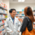 Pharmacist consulting a patient about cold sore treatment in a modern, bright pharmacy with shelves of medication and health products.