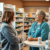 Pharmacist consulting a patient about cough treatment in a modern pharmacy with medicine shelves in the background.