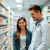 A modern pharmacy interior with a pharmacist assisting a patient, surrounded by shelves of medications and health products.