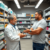 A modern pharmacy interior with shelves of hair care products and medications, a pharmacist consulting with a man about hair loss treatment options.
