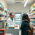 Bright community pharmacy interior with a pharmacist consulting a patient at the counter, surrounded by shelves of medicines and health products.