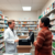 Bright community pharmacy interior with a pharmacist consulting a patient at the counter, surrounded by shelves of medications and health products.