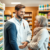 Pharmacist consulting a patient about joint and muscle pain relief in a modern pharmacy with shelves of medications and health products.