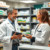 Pharmacist consulting a patient in a modern pharmacy, surrounded by shelves of medications and health products.