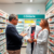 A man talks to a female pharmacist in a pharmacy aisle lined with medicine shelves. A mannequin wearing a doctor’s coat and stethoscope stands between them under a sign reading “COntarie.”. Pharmacist consulting with a patient about stomach health in a modern pharmacy with medication shelves and gastrointestinal care symbols.